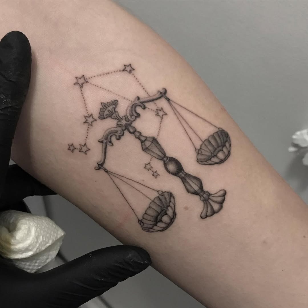 This tattoo features a beautifully detailed Libra scale, elegantly poised between two shell designs.