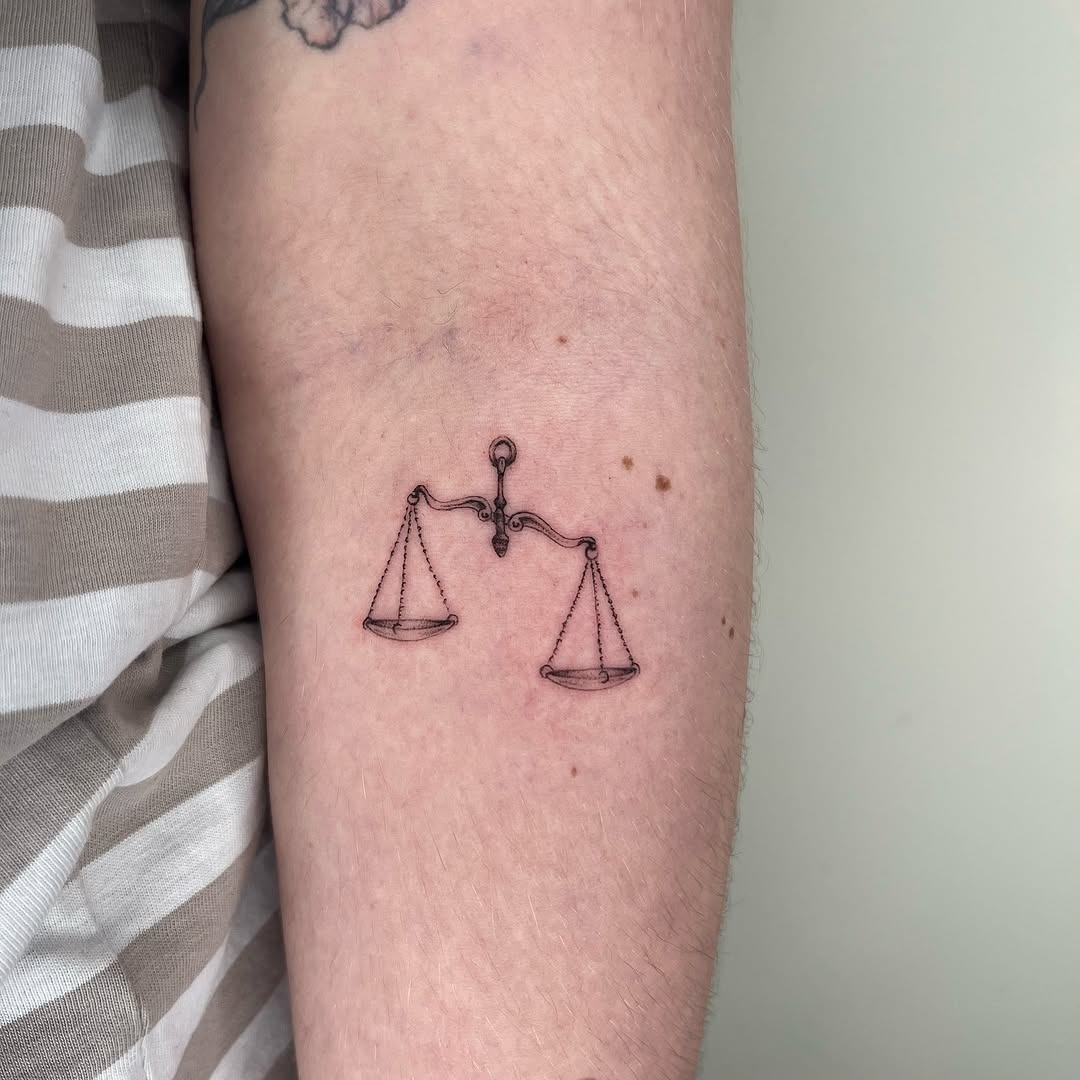 This tattoo showcases a delicate depiction of the Libra scales, symbolizing balance and harmony.