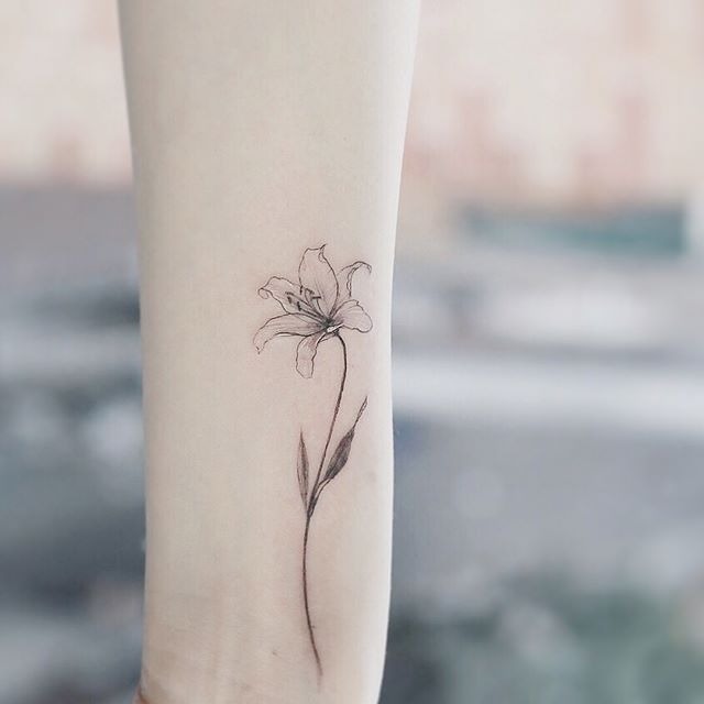 This fine-line lily tattoo embraces simplicity, featuring a minimalistic design with thin, delicate lines.
