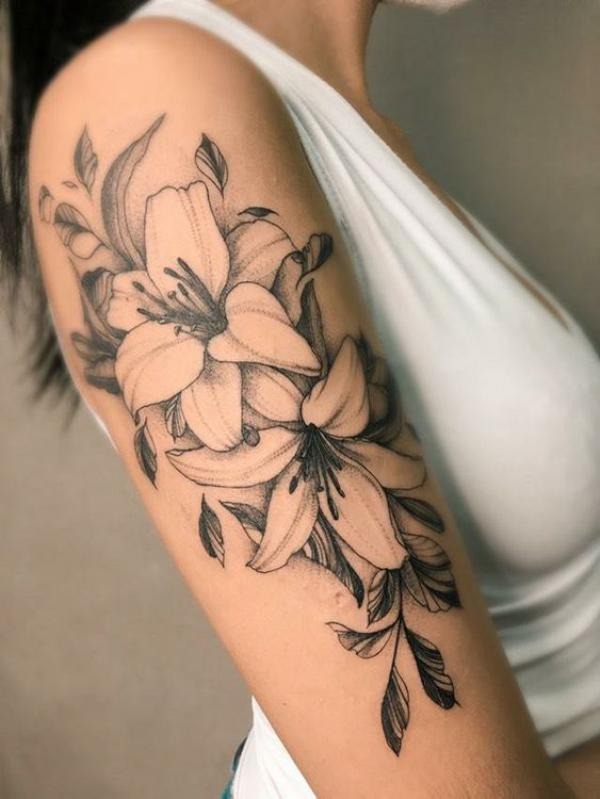 This shoulder tattoo features multiple lilies intertwined with leaves, creating a stunning and detailed floral arrangement.
