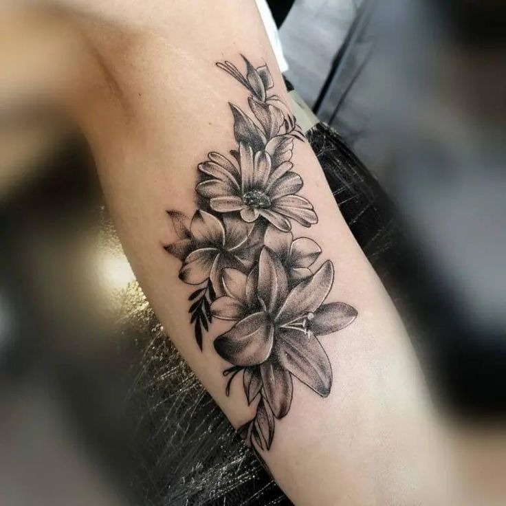 This arm tattoo combines the delicate beauty of lilies with the cheerful presence of daisies, creating a stunning floral arrangement.