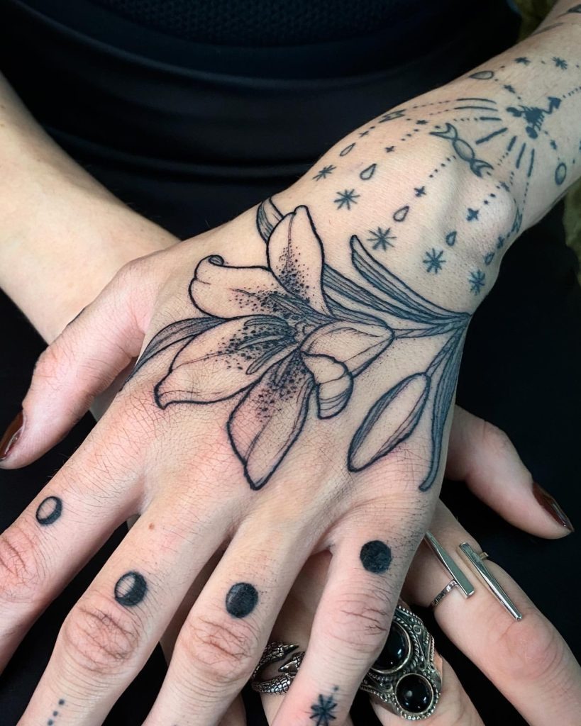 This lily hand tattoo is beautifully unique, blending traditional floral elements with celestial symbols.