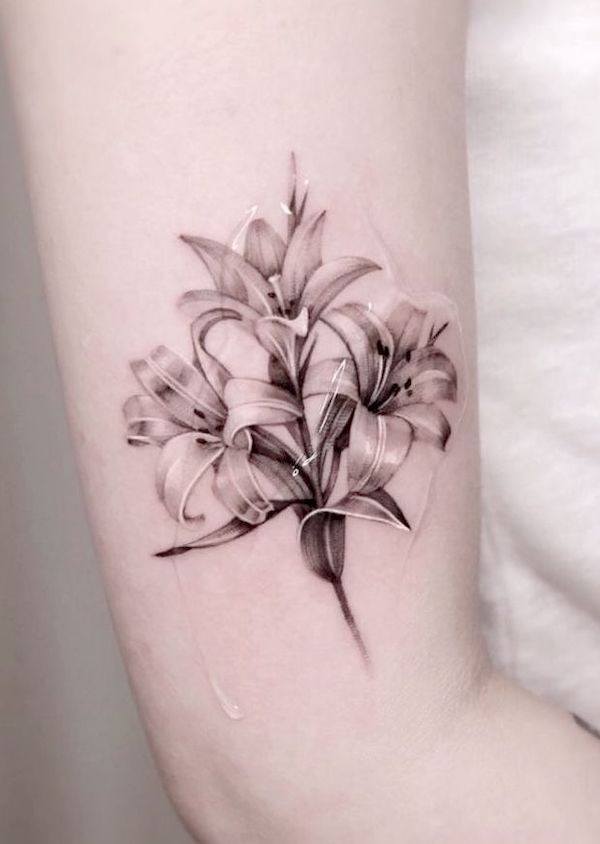 This forearm tattoo features multiple lilies in soft, gradient tones, giving the tattoo a watercolor-like effect.