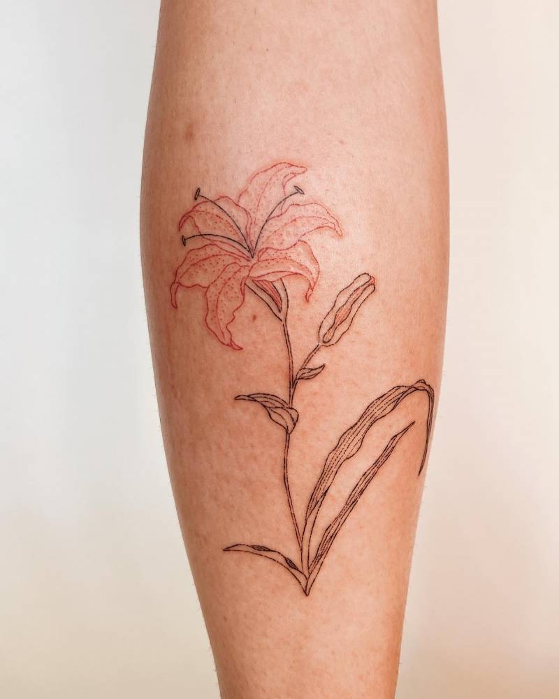 This calf tattoo features a single lily drawn with minimalistic outlines and soft shading, creating a clean and natural look.