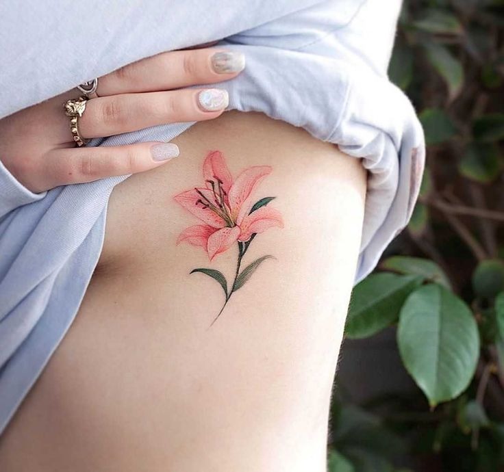 This ribcage tattoo beautifully showcases a single pink lily with soft shading, highlighting the flower's natural beauty.