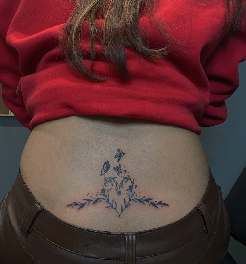 This lower back tattoo features a delicate floral design surrounded by fluttering butterflies.