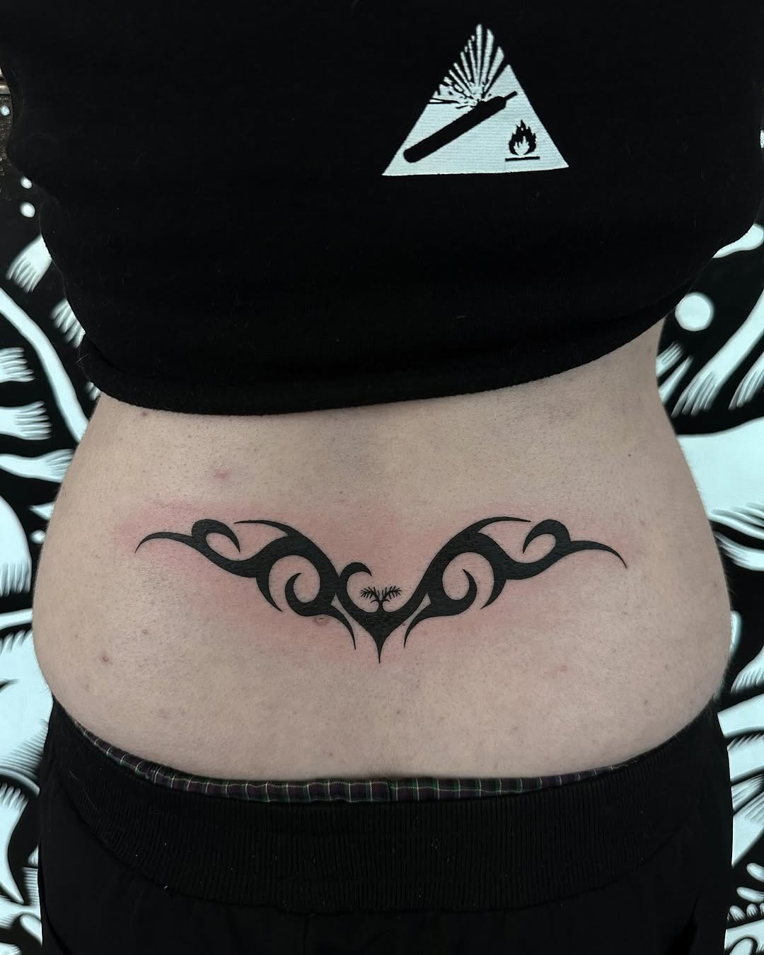 This lower back tattoo features stylish black curves that create an elegant and flowing design.