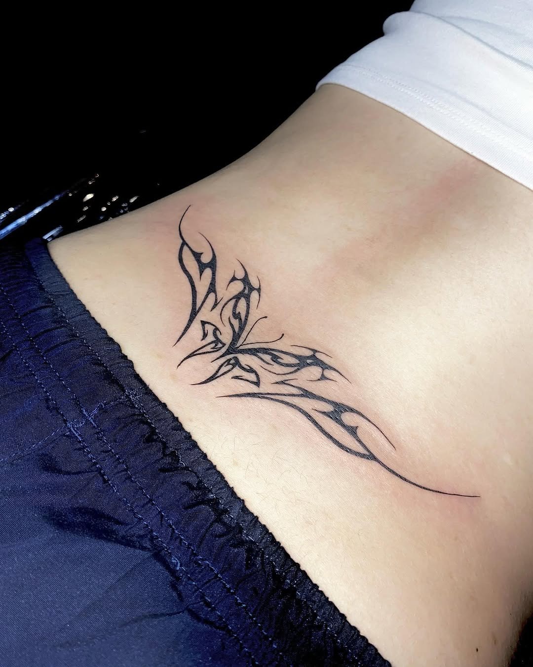 This striking tattoo features a beautifully designed butterfly etched in black ink on the lower back.
