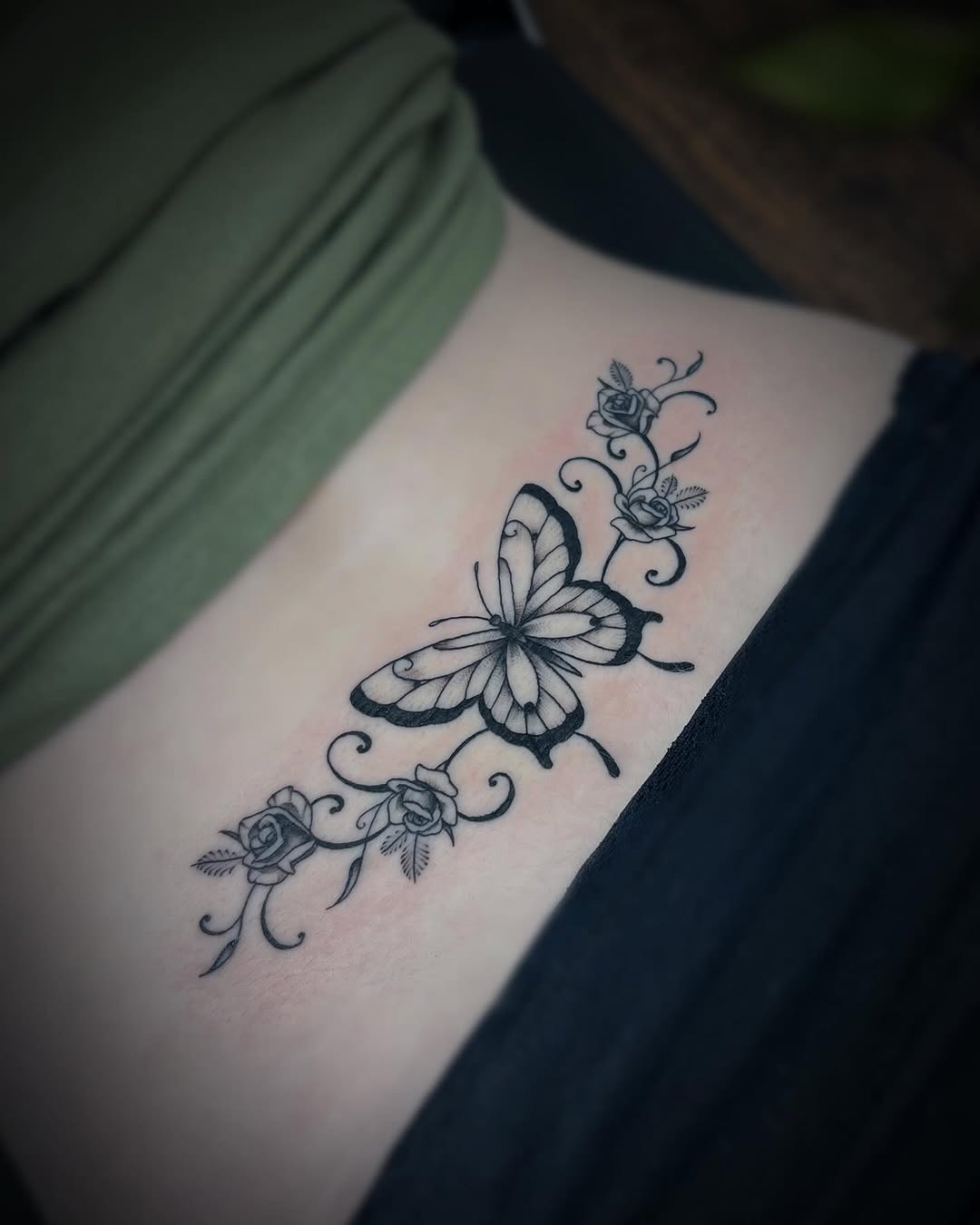 This lower back tattoo features a striking butterfly surrounded by delicate roses and swirling vines.