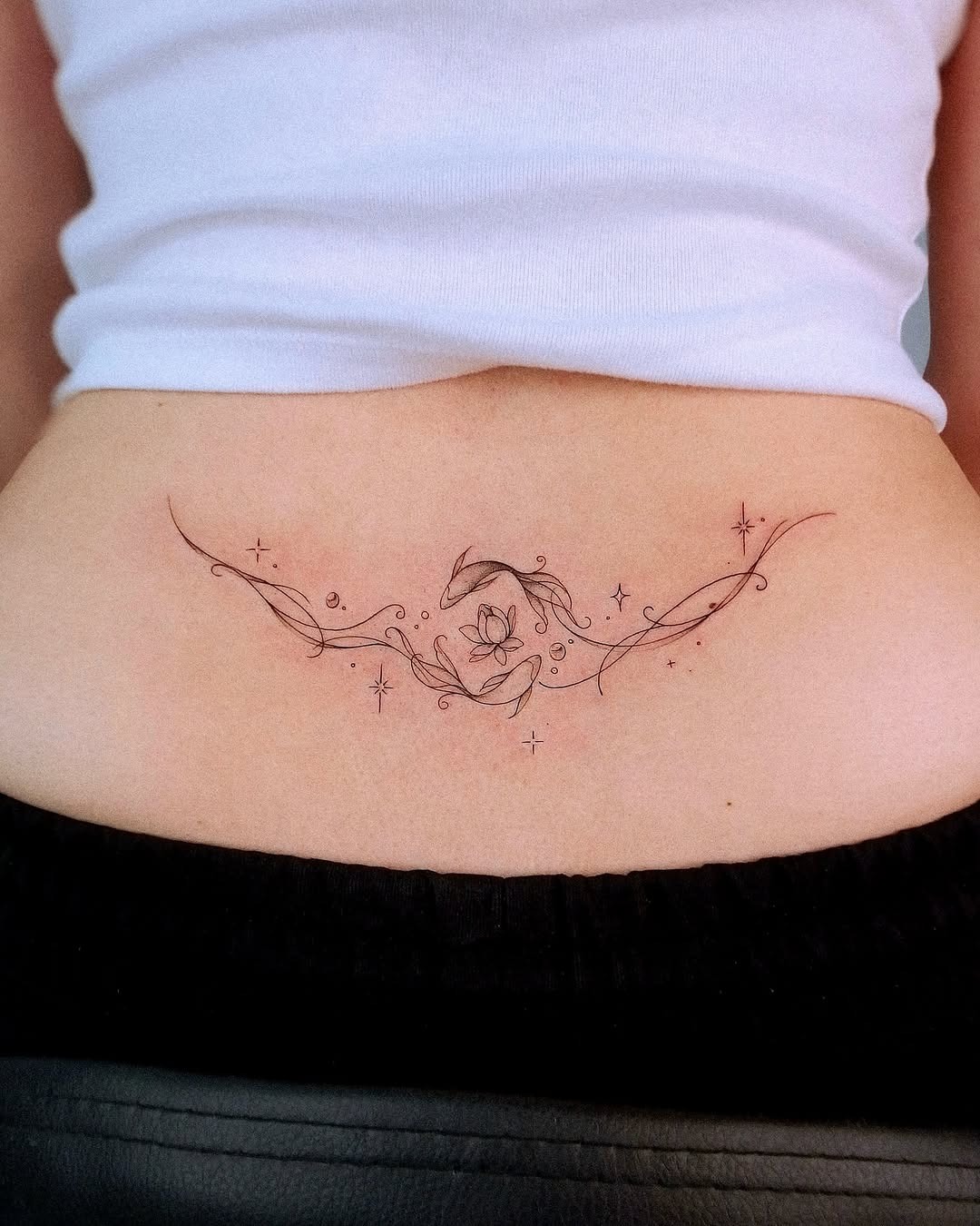 This lower back tattoo features an elegant floral design intertwined with delicate lines and star-like accents.