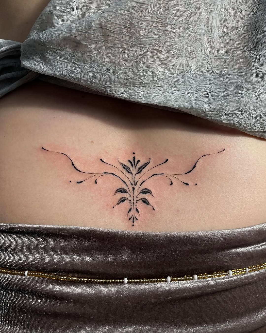 This tattoo features a delicate floral pattern that adds a touch of elegance to the lower back.