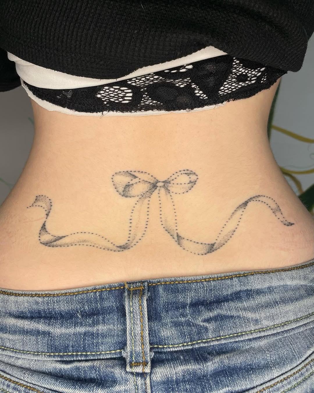 This stunning lower back tattoo features a delicate ribbon design, creating a charming and feminine vibe.
