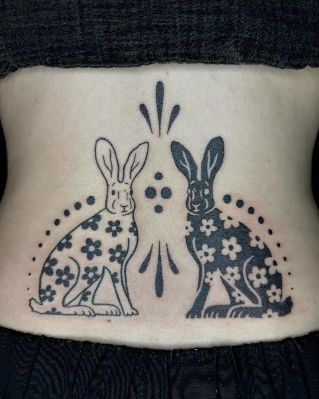 This lower back tattoo features two charming rabbits adorned with intricate floral designs.