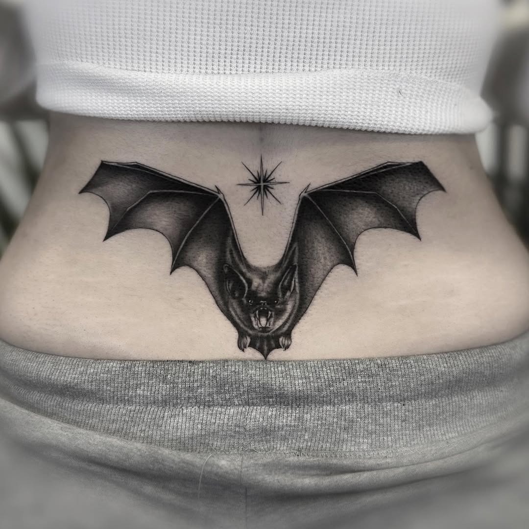 This captivating lower back tattoo features a detailed bat with intricately designed wings stretched wide.