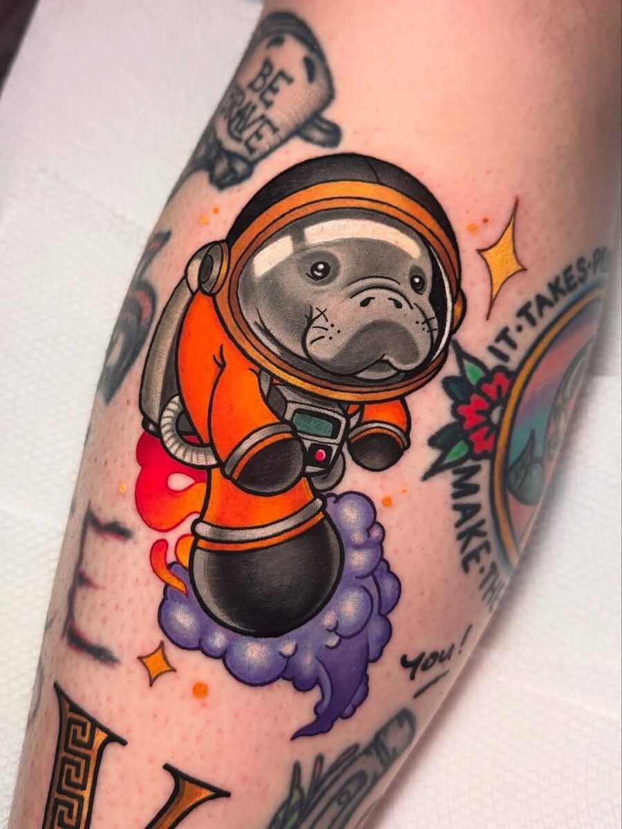 This tattoo features a charming manatee dressed as an astronaut, floating through a colorful space scene.