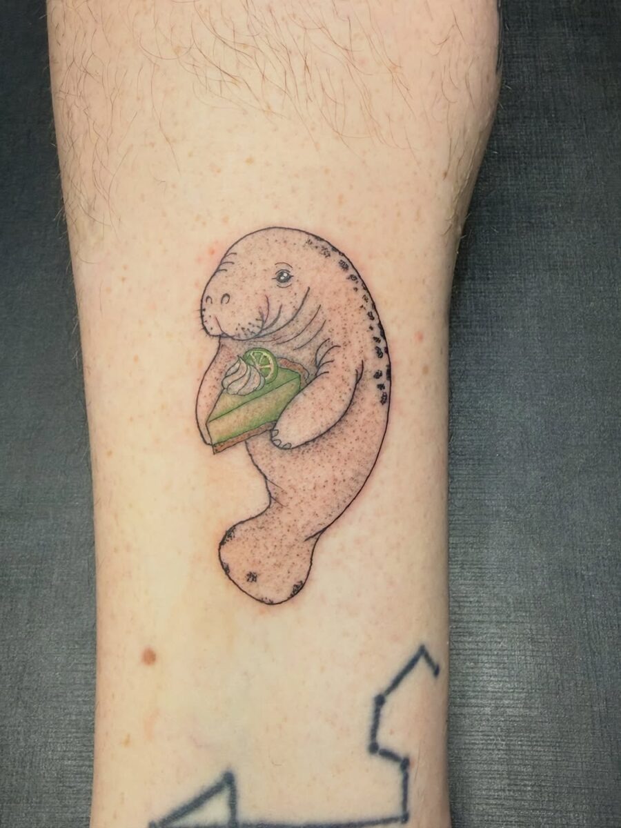 This charming tattoo showcases a playful manatee cradling a slice of cake.