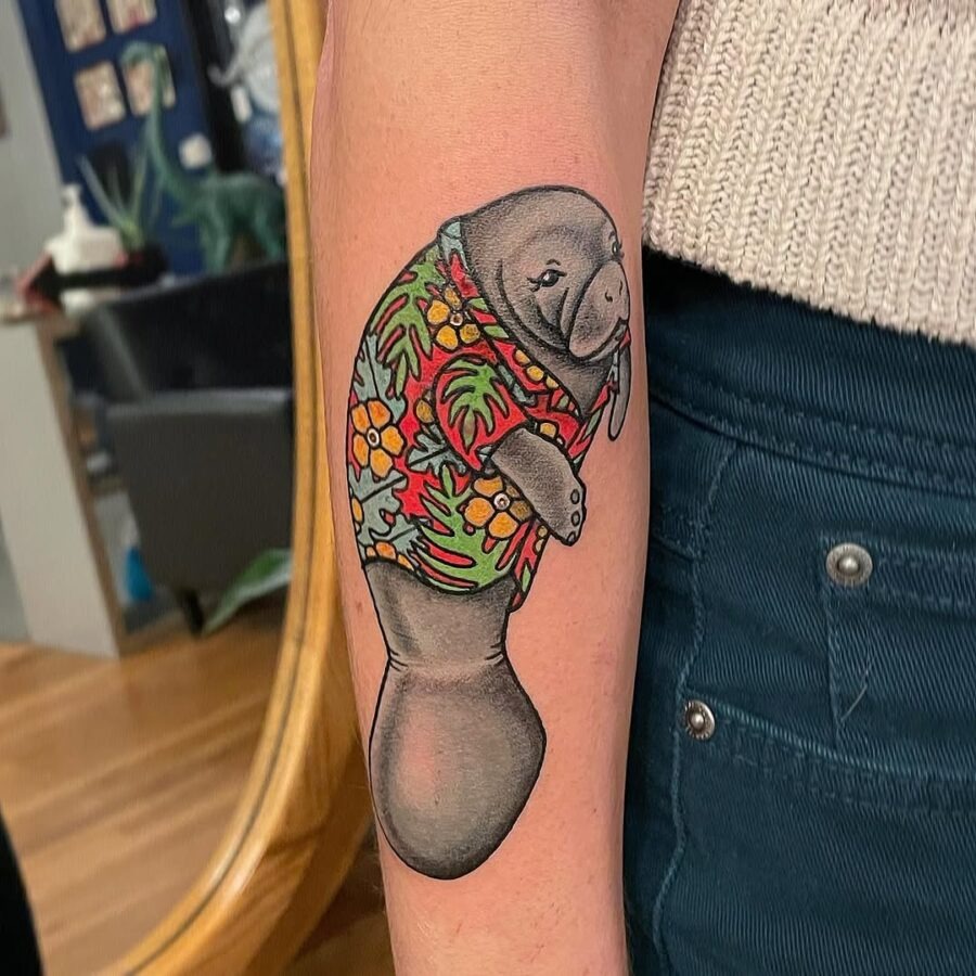 This tattoo features a playful manatee adorned in a Hawaiian shirt, exuding a relaxed tropical vibe.