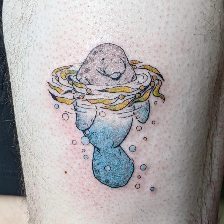 This tattoo features an adorable manatee surrounded by playful turquoise water and flowing seaweed.