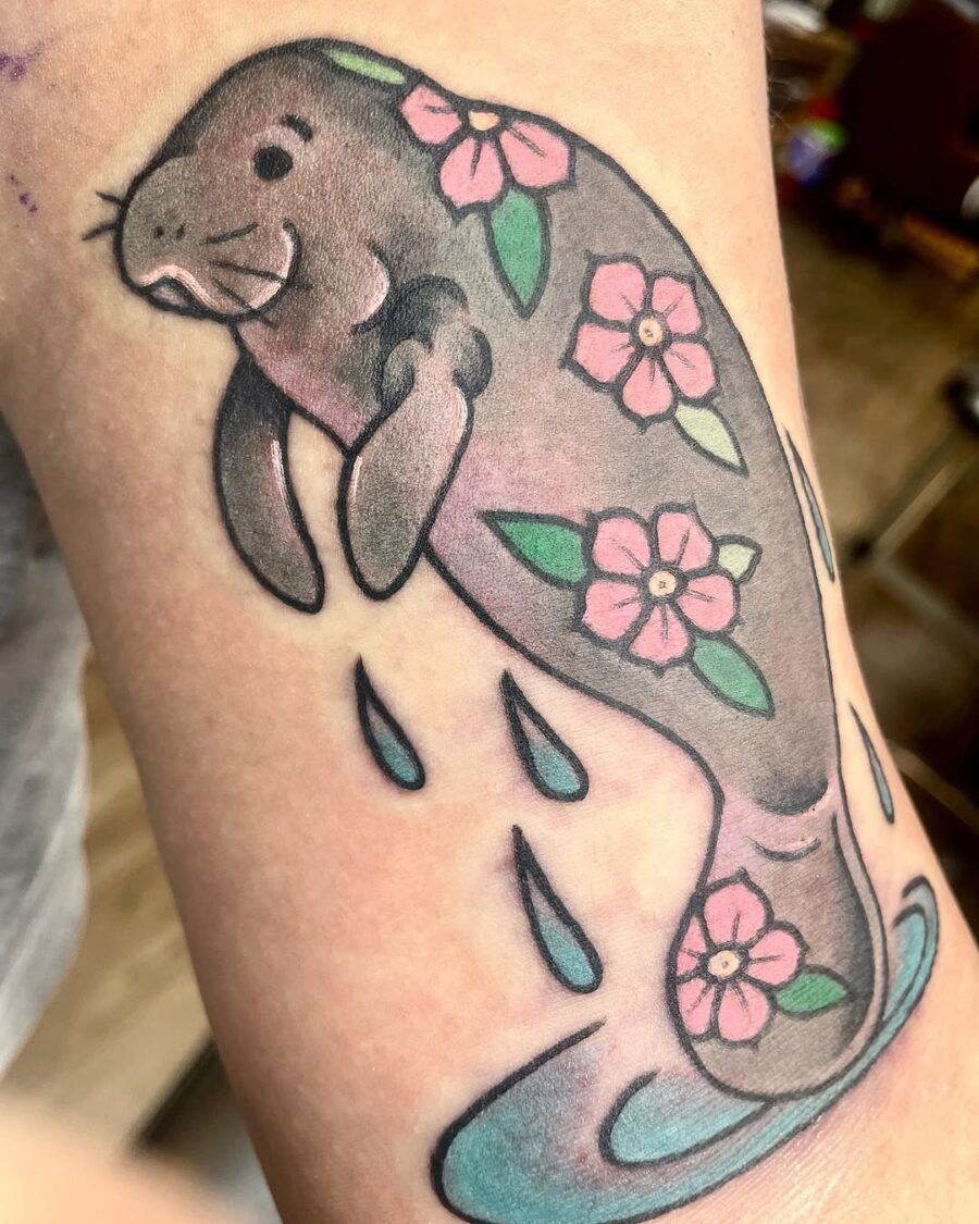 This delightful manatee tattoo showcases a playful design with flowers and water droplets.