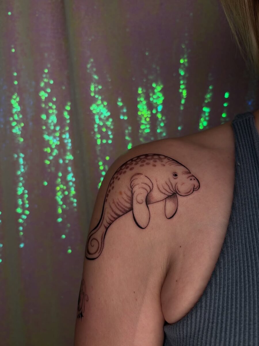 This lovely manatee tattoo graces a shoulder, combining whimsical design with a touch of humor.
