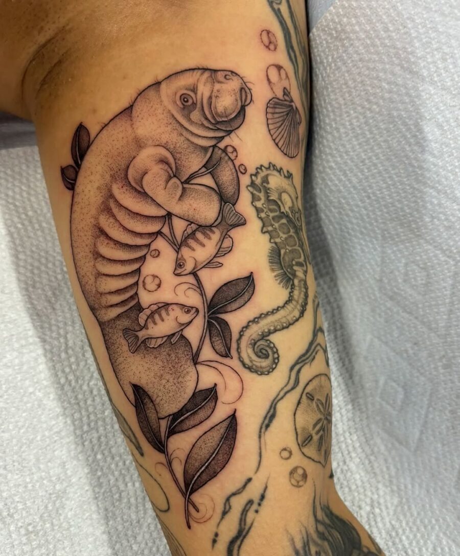 This stunning tattoo features a playful manatee, artistically entwined with fish and foliage.
