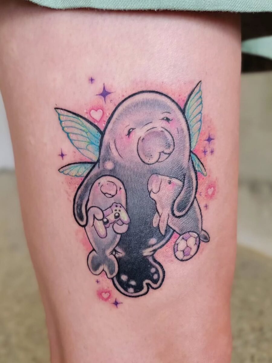 This tattoo showcases a whimsical manatee adorned with delicate fairy wings, cradling two cute baby manatees.