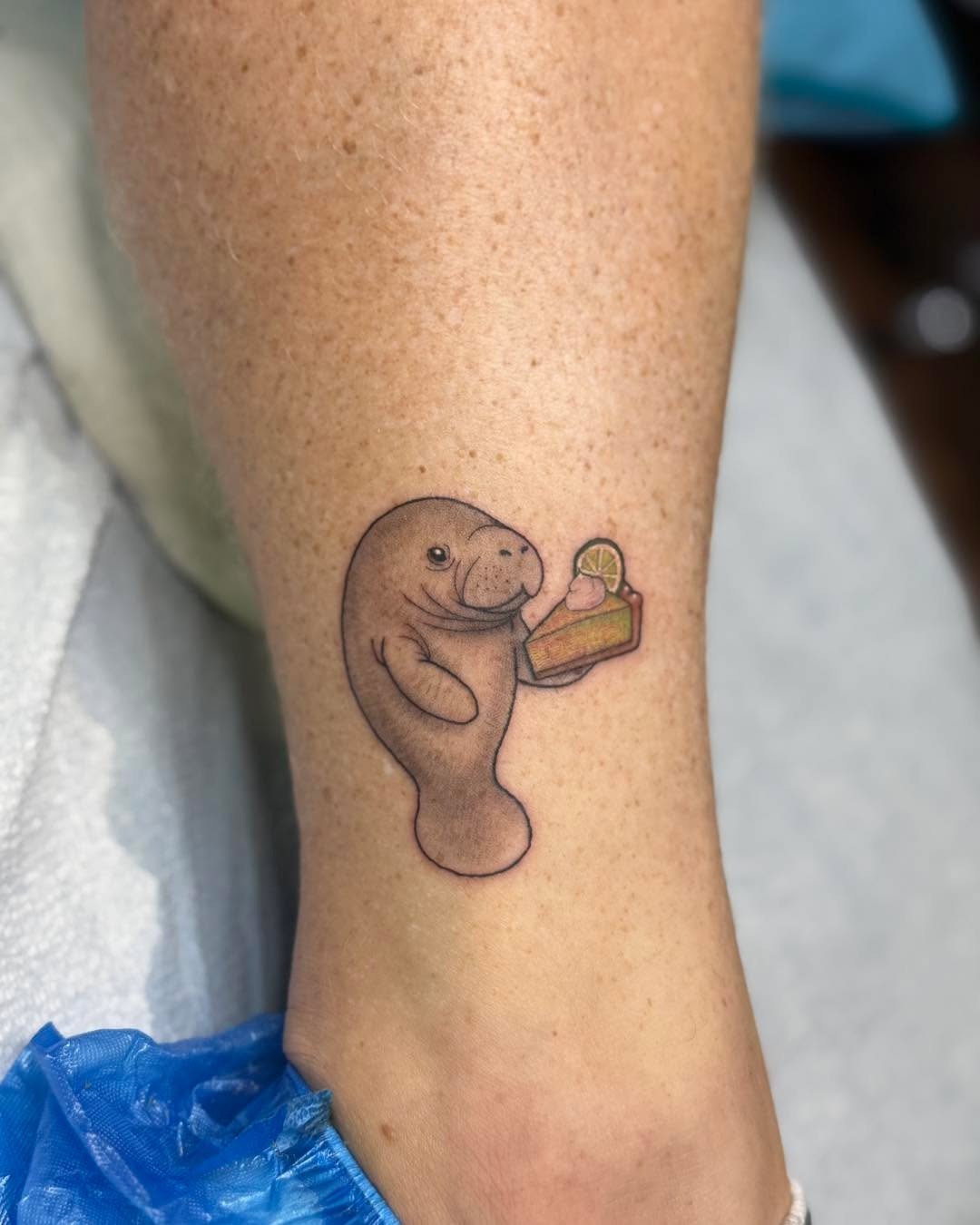 This adorable tattoo features a cheerful manatee holding a snack.