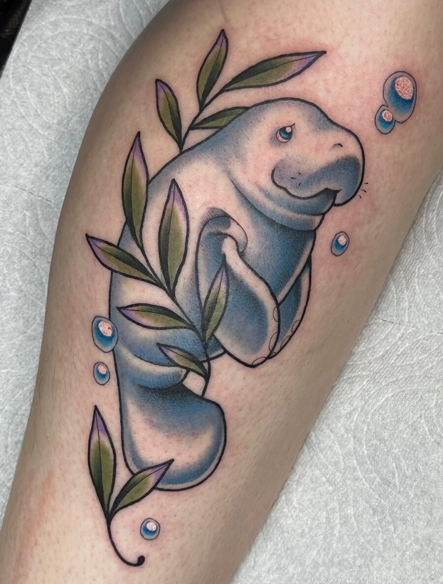 This delightful manatee tattoo blends soft colors with leafy details for a serene vibe.