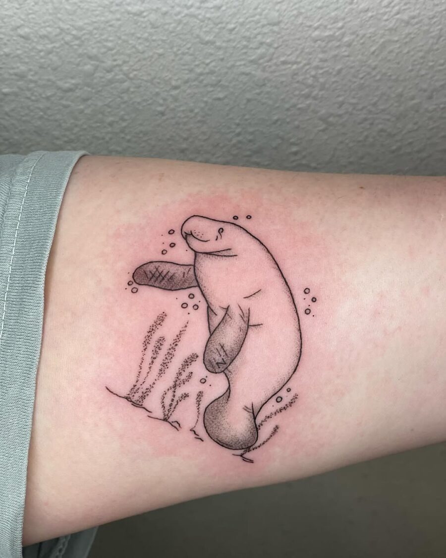 This tattoo features a playful manatee surrounded by bubbles and seaweed.