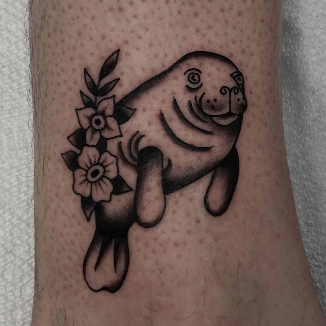 This tattoo features a playful manatee surrounded by beautiful flowers.