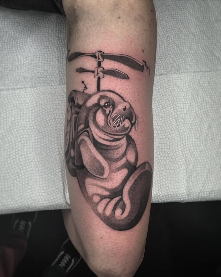 This tattoo features a cute manatee, rendered in sleek black and gray hues.