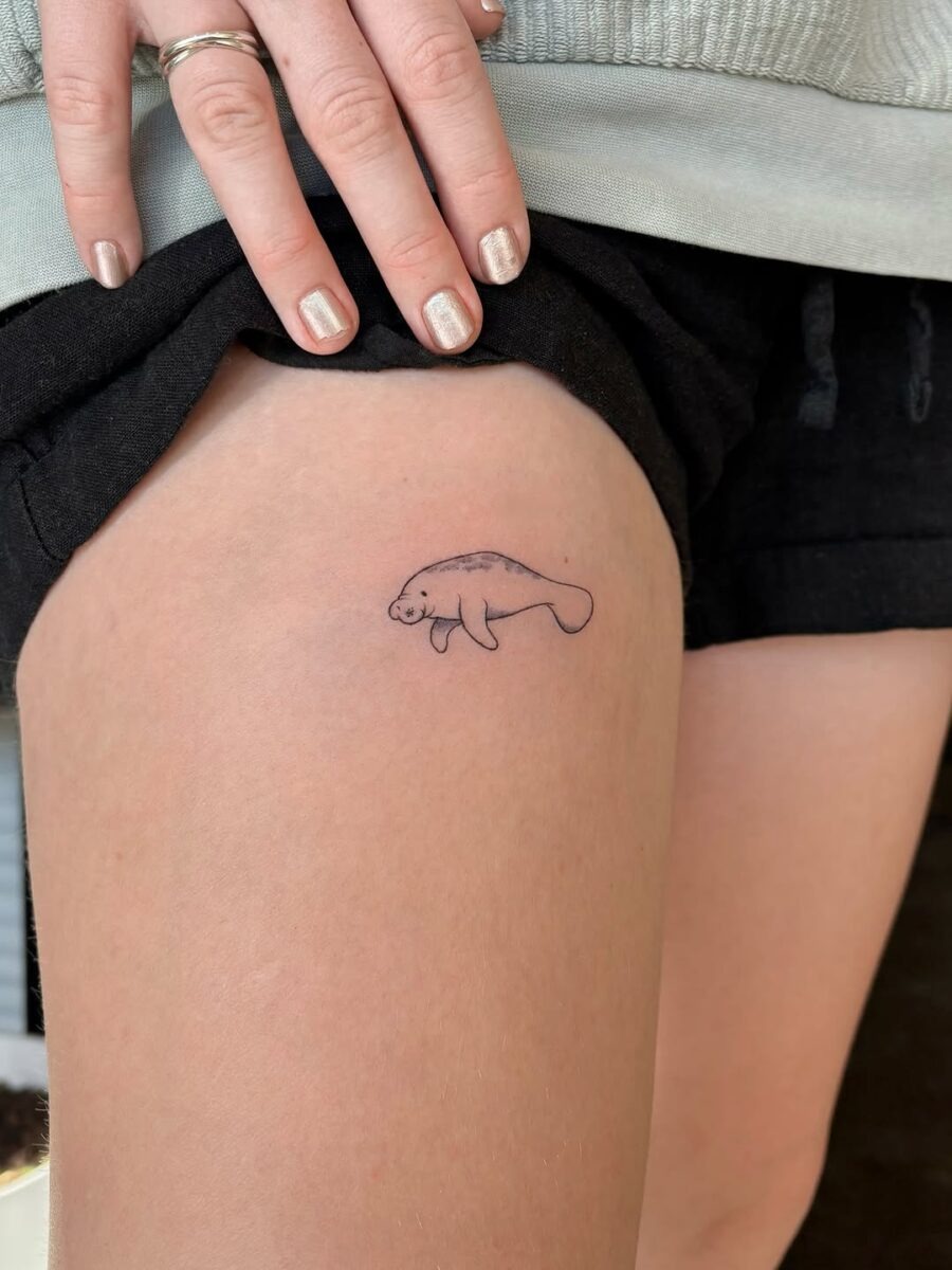 This tattoo features a small, delicate manatee design on the thigh, embodying a playful and serene vibe.