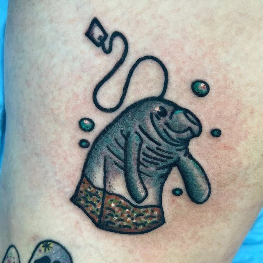 This playful tattoo features a cartoonish manatee wearing shorts, radiating charm and fun.