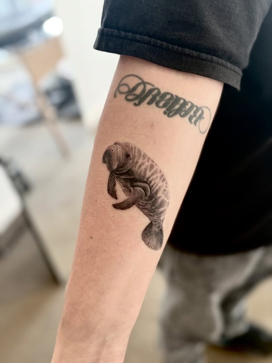 This tattoo features a beautifully detailed manatee, rendered in black and gray ink.