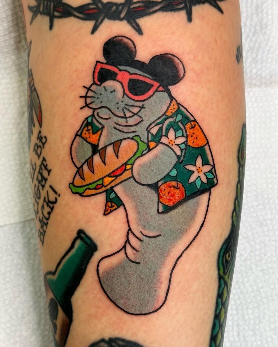 This charming tattoo features a cartoon manatee sporting a Hawaiian shirt and sunglasses, holding a sandwich.