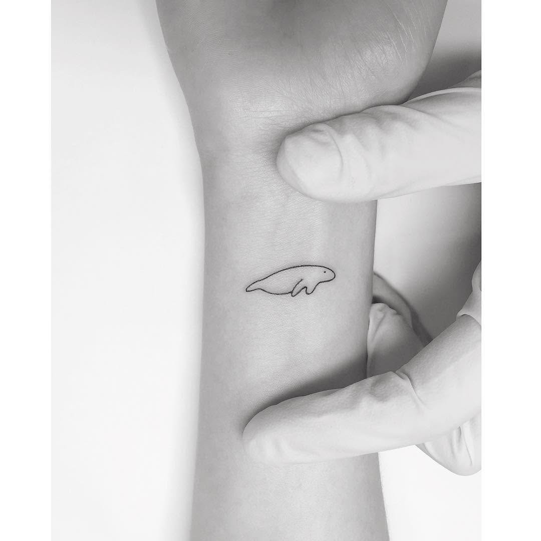 This delicate tattoo showcases a simple outline of a manatee, perfectly inked on the wrist.