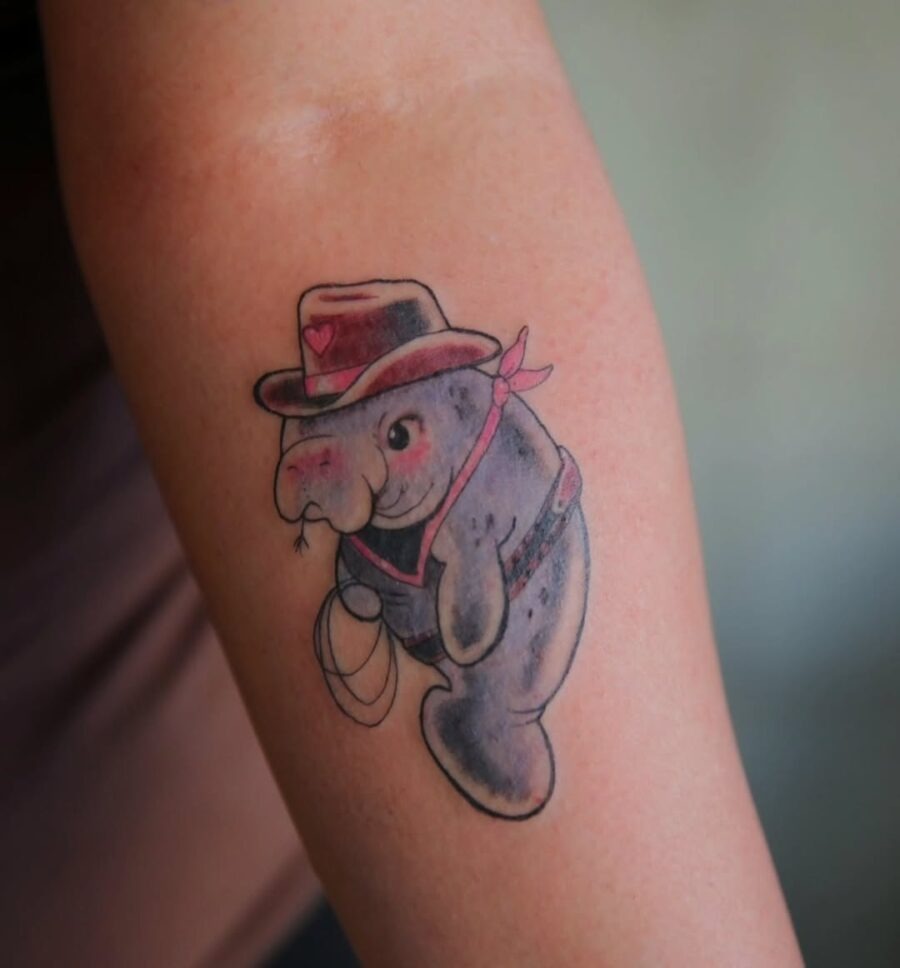 This charming manatee tattoo features a whimsical cowboy hat and a playful expression.