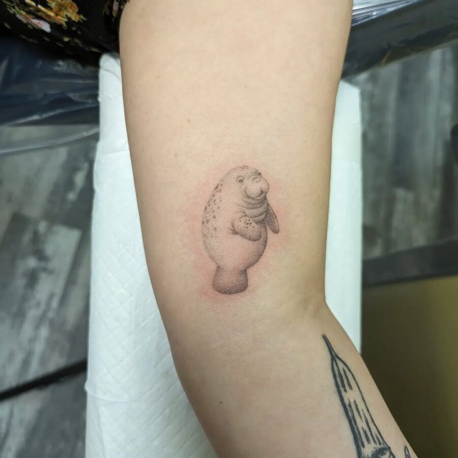 This playful manatee tattoo showcases a whimsical design that adds a touch of joy to any arm.