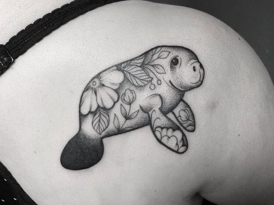 This delightful tattoo features a playful manatee surrounded by intricate floral designs.