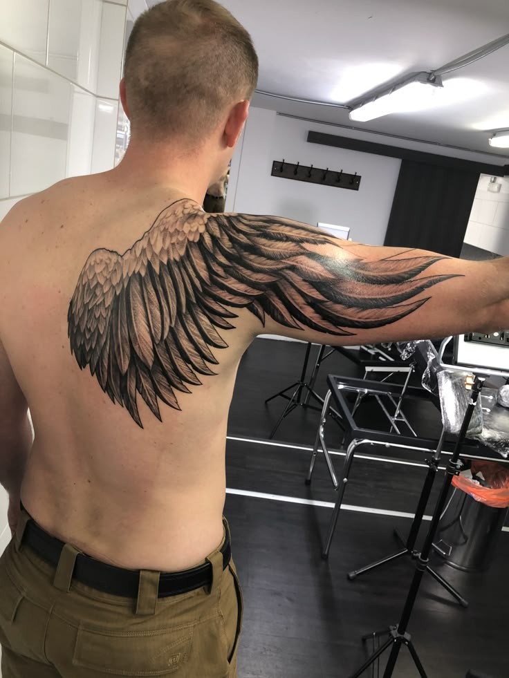 This tattoo cleverly integrates the shoulder blade and upper arm, creating a smooth design that wraps the body like an actual wing in flight.