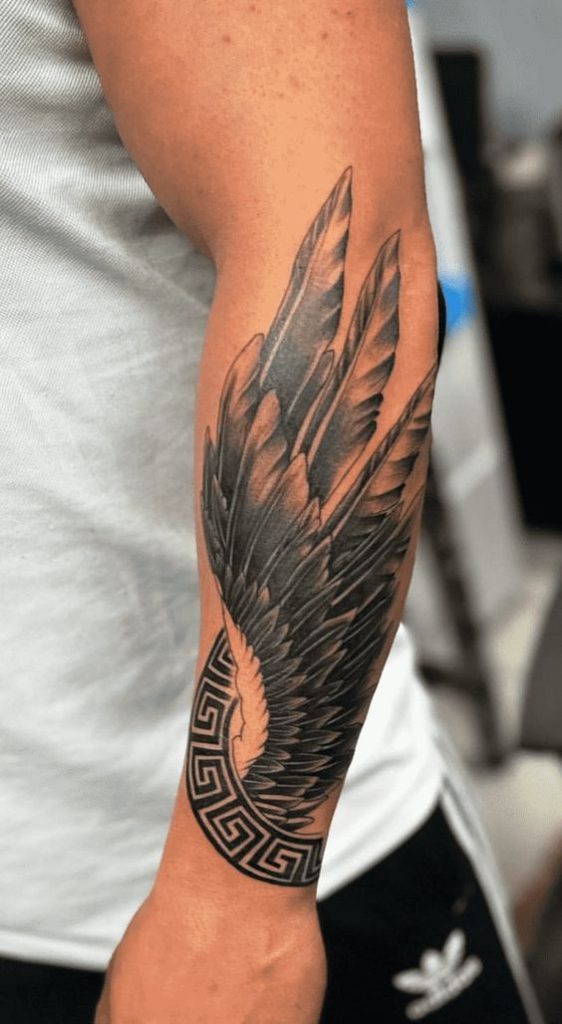 Blending myth and power, this forearm tattoo fuses feather realism with a classic Greek key pattern at the base.
