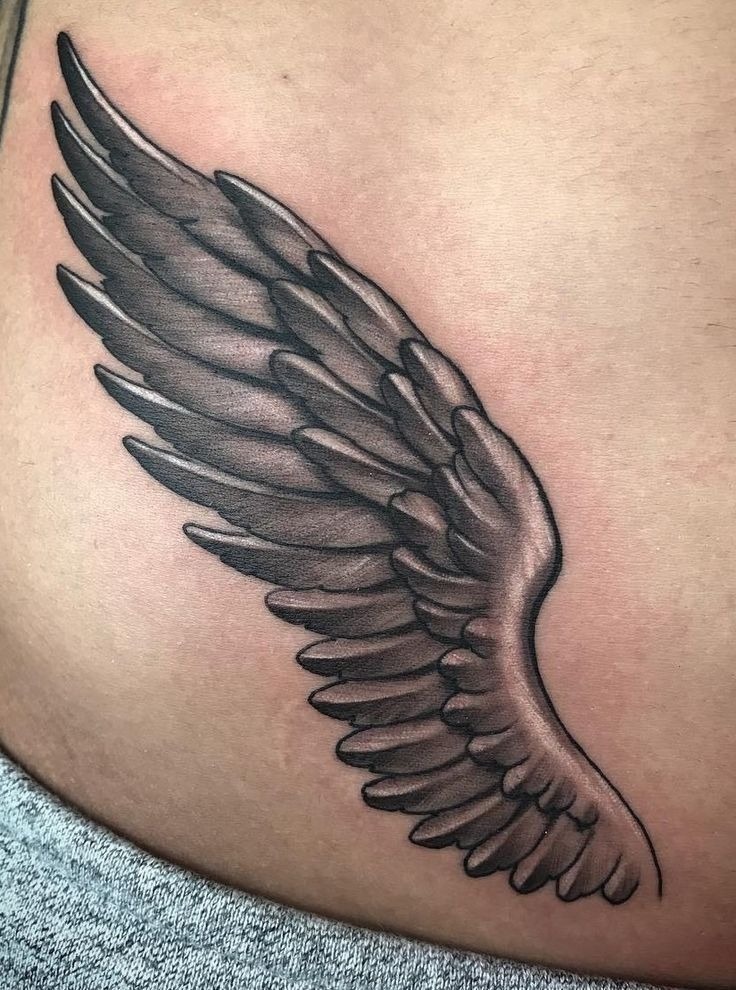 For something more discreet yet meaningful, this ribcage tattoo showcases a single wing in soft grayscale.