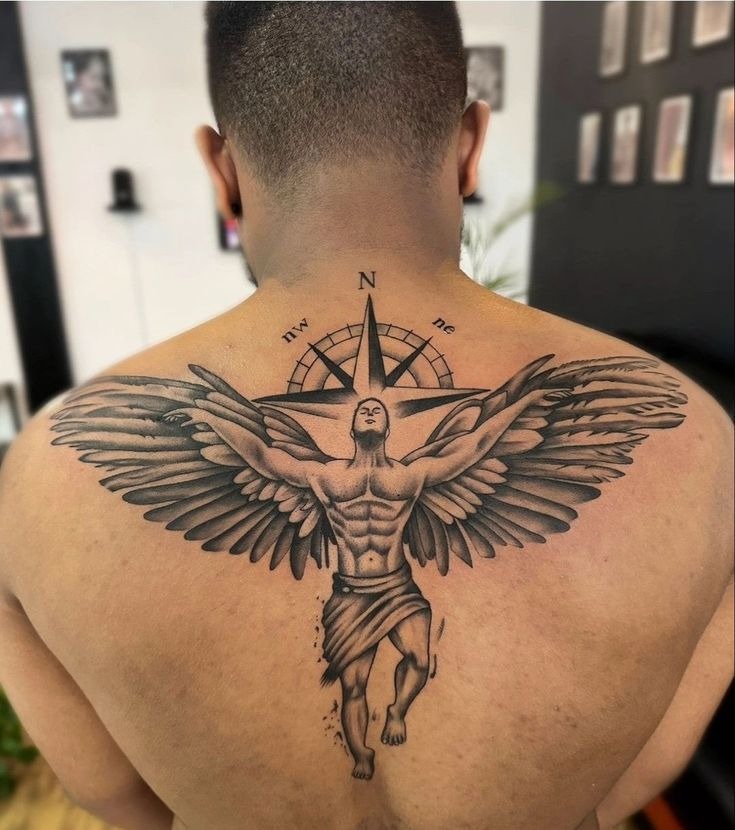 A commanding back tattoo featuring a stylized angel rising toward a compass, arms and wings extended in perfect symmetry.
