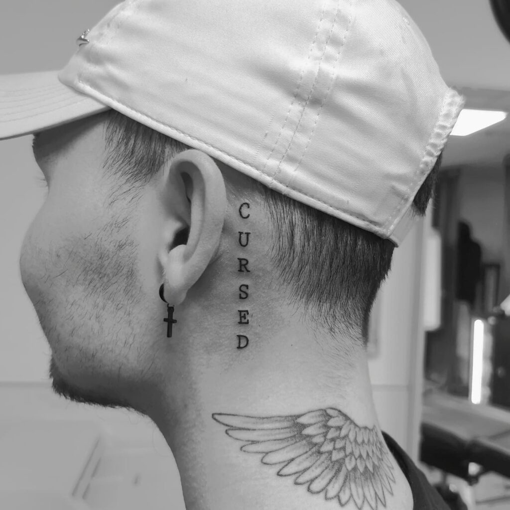 Vertical “Cursed” Lettering Behind the Ear Tattoo Design