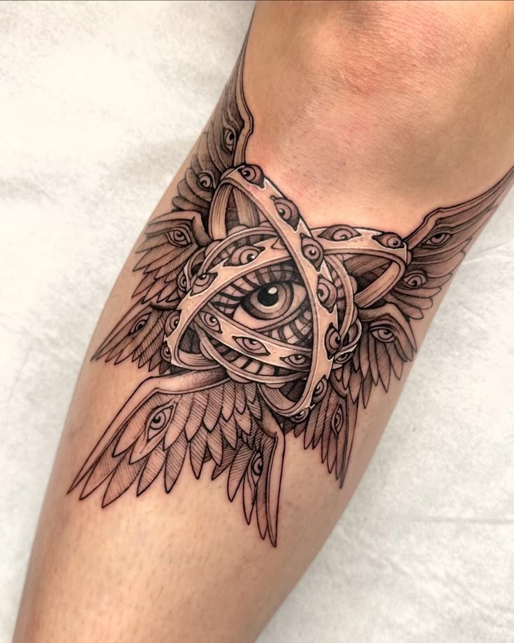 Combining elements of ancient mysticism and divine symbolism, this tattoo features a central eye enclosed in flowing, ornate bands that mimic wings and layered feathers.