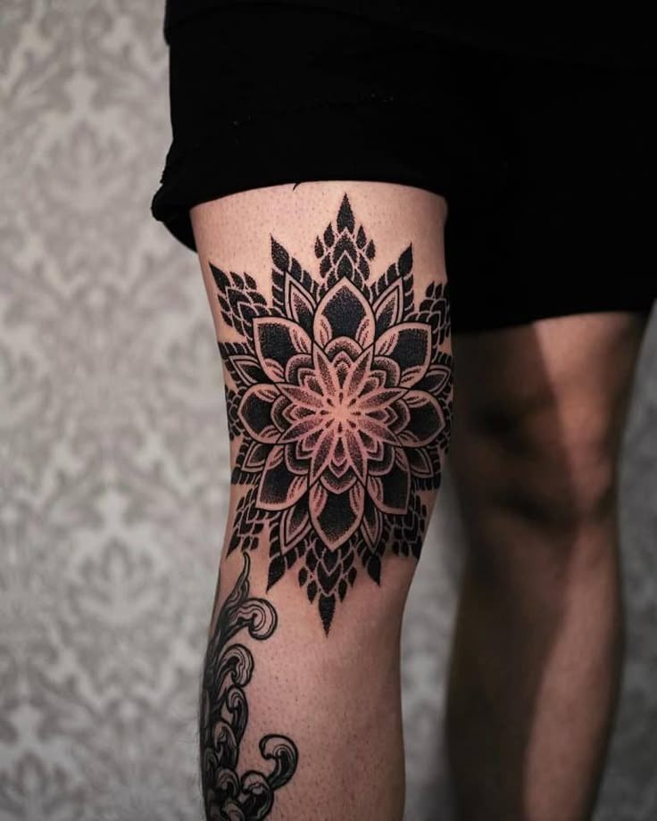 Bold blackwork defines this mandala tattoo wrapping around the upper leg and knee.