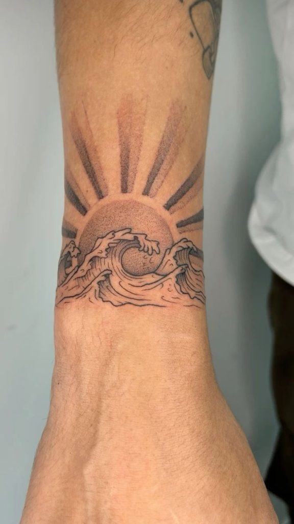 The sun rises above stylized waves in this stunning wristband tattoo.