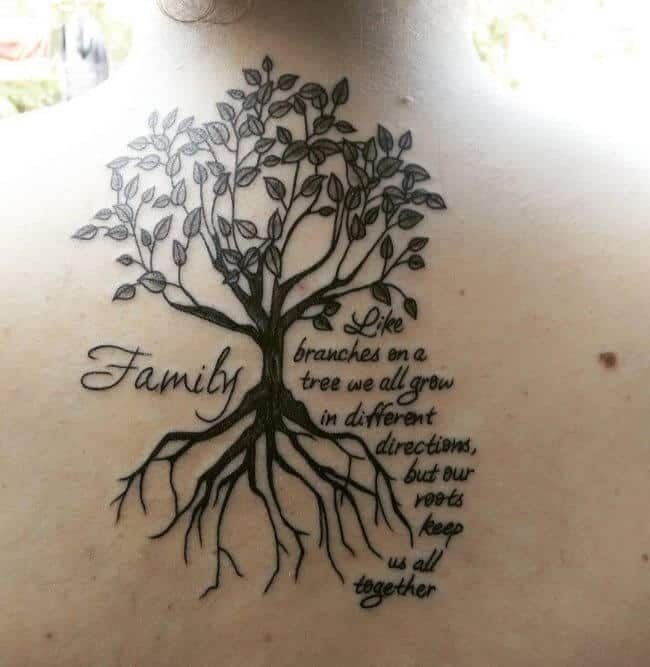 This back tattoo features a delicate tree with detailed roots and branches, accompanied by the text: "Like branches on a tree we all grow in different directions, but our roots keep us all together." The message, paired with the simple line work of the tree, emphasizes the theme of family unity despite physical or emotional distance.