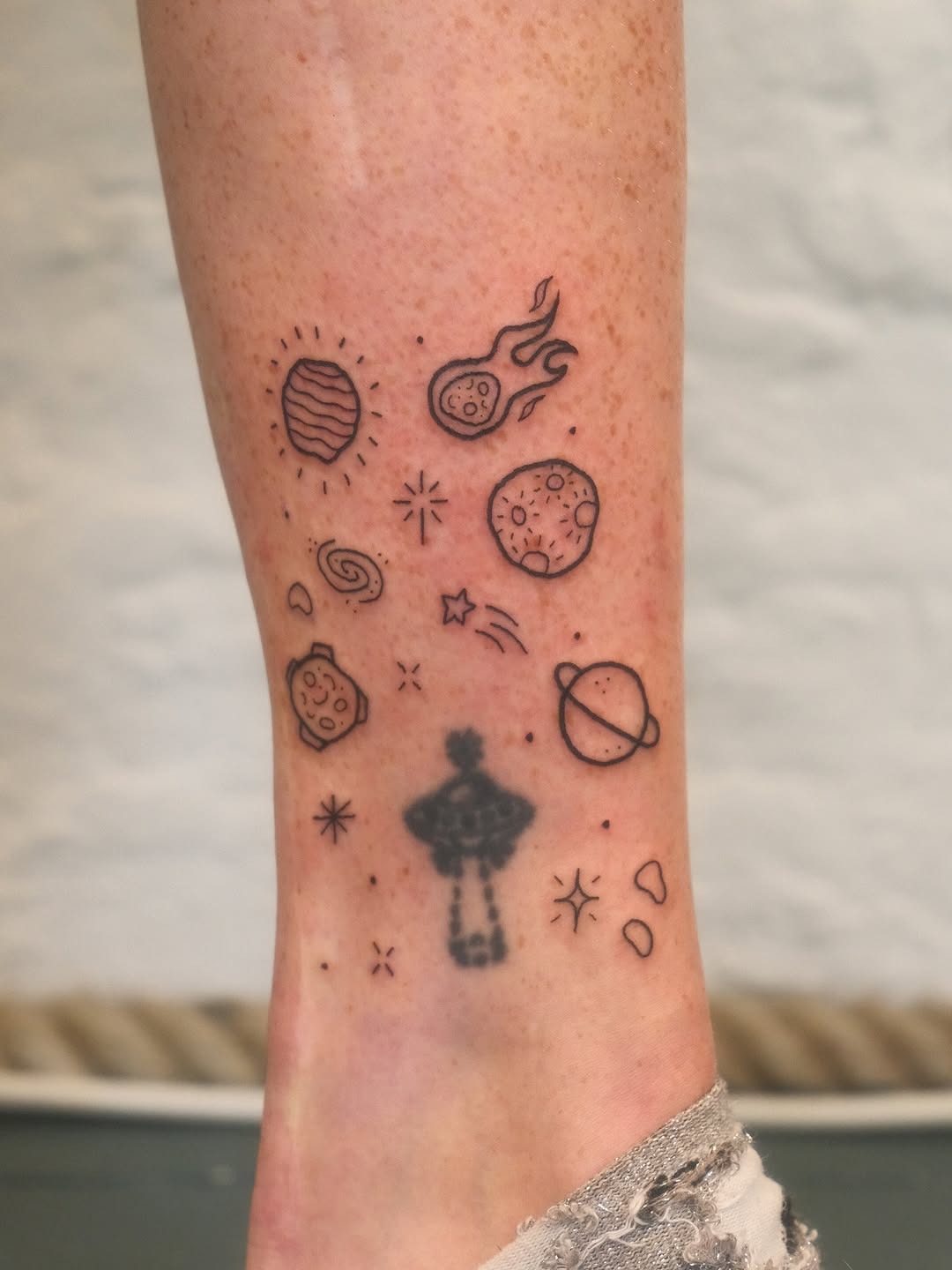 This tattoo design showcases a playful array of celestial elements, including meteors, planets, and swirling galaxies.