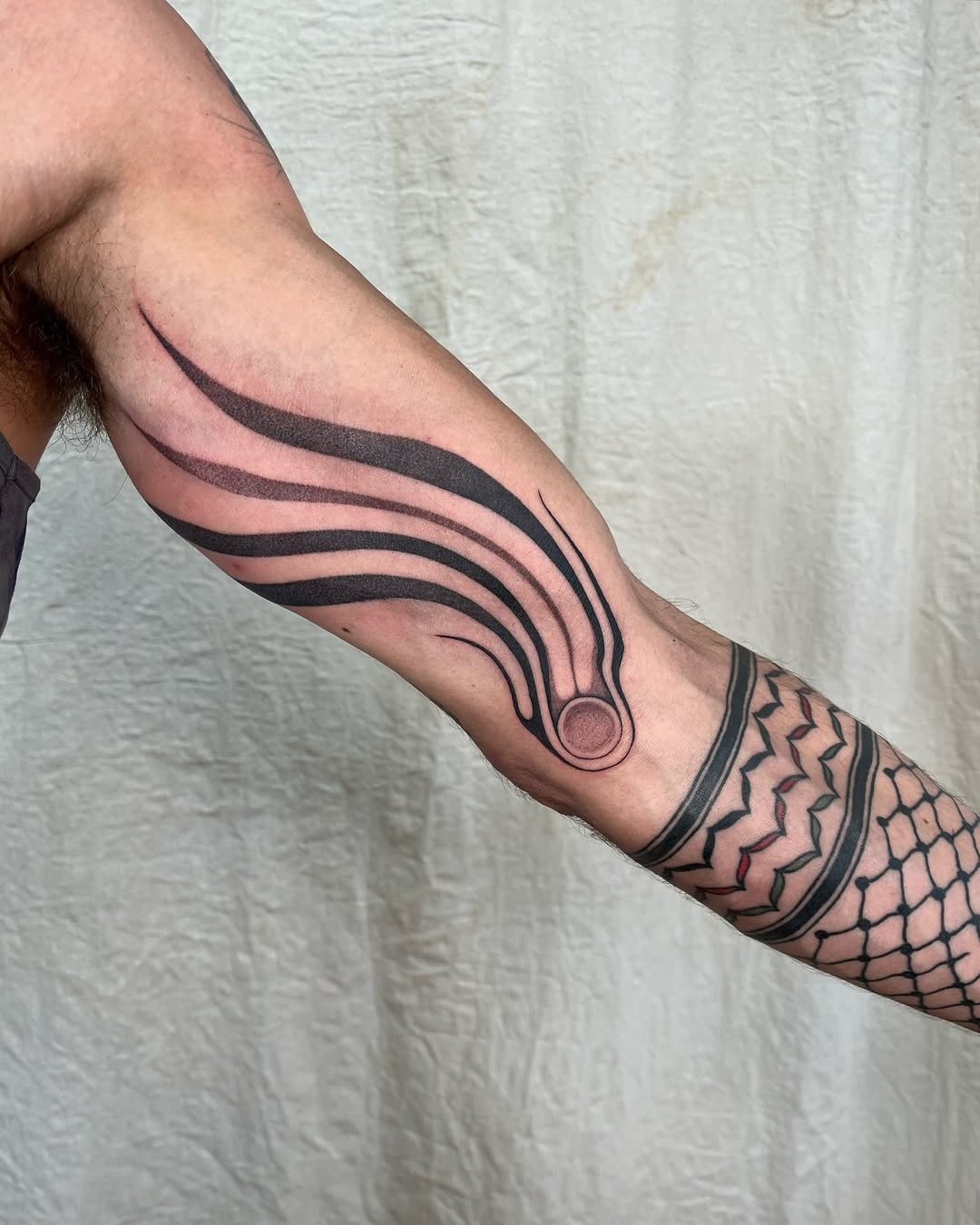 This tattoo features sleek, elongated lines resembling a meteor's trail, elegantly wrapping around the arm.